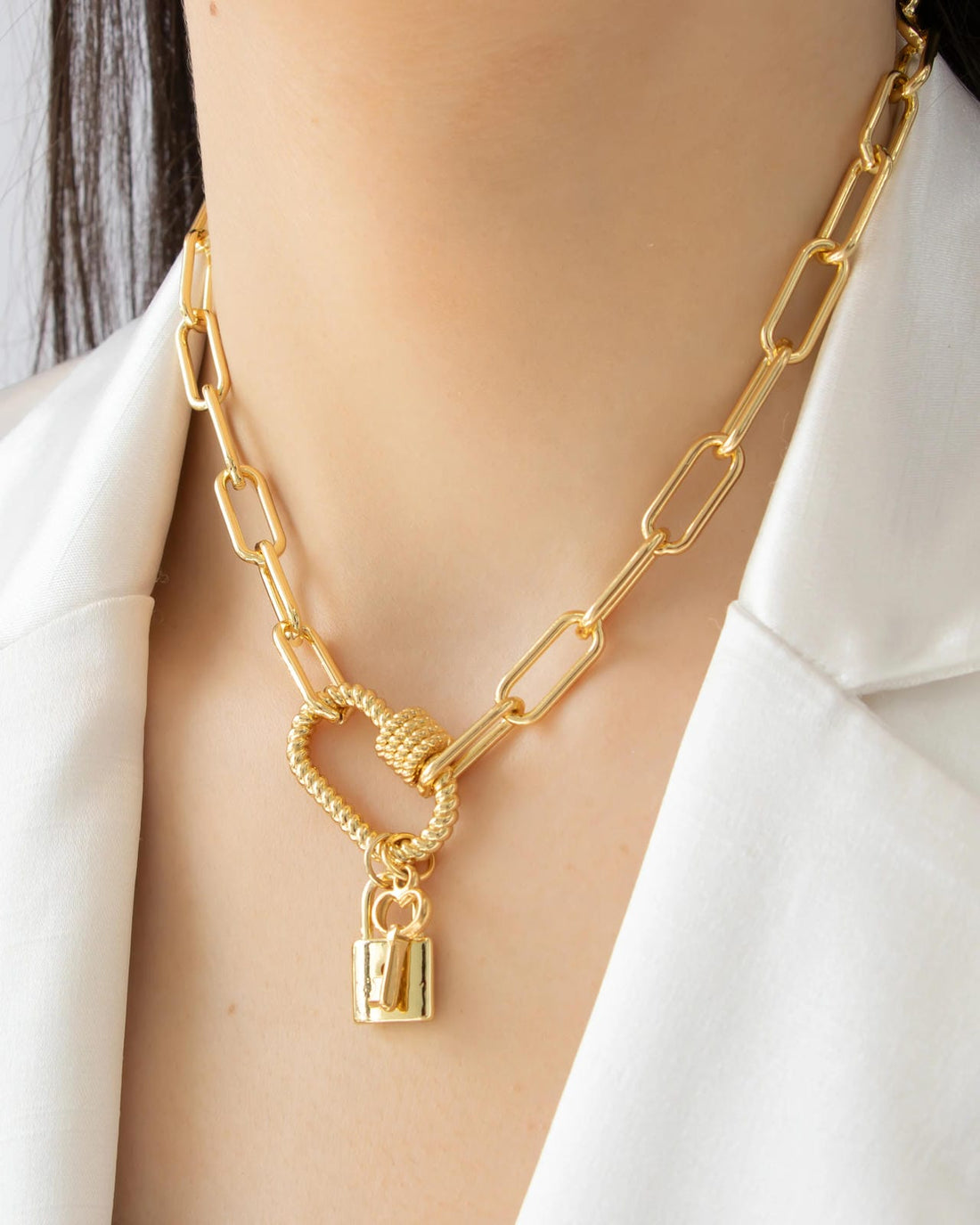 Gold chain necklace with a lock pendant on a person wearing a white blazer.