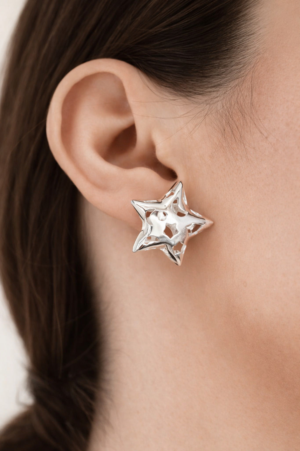 Model wearing silver-plated hollow star stud earrings with polished finish and modern geometric design