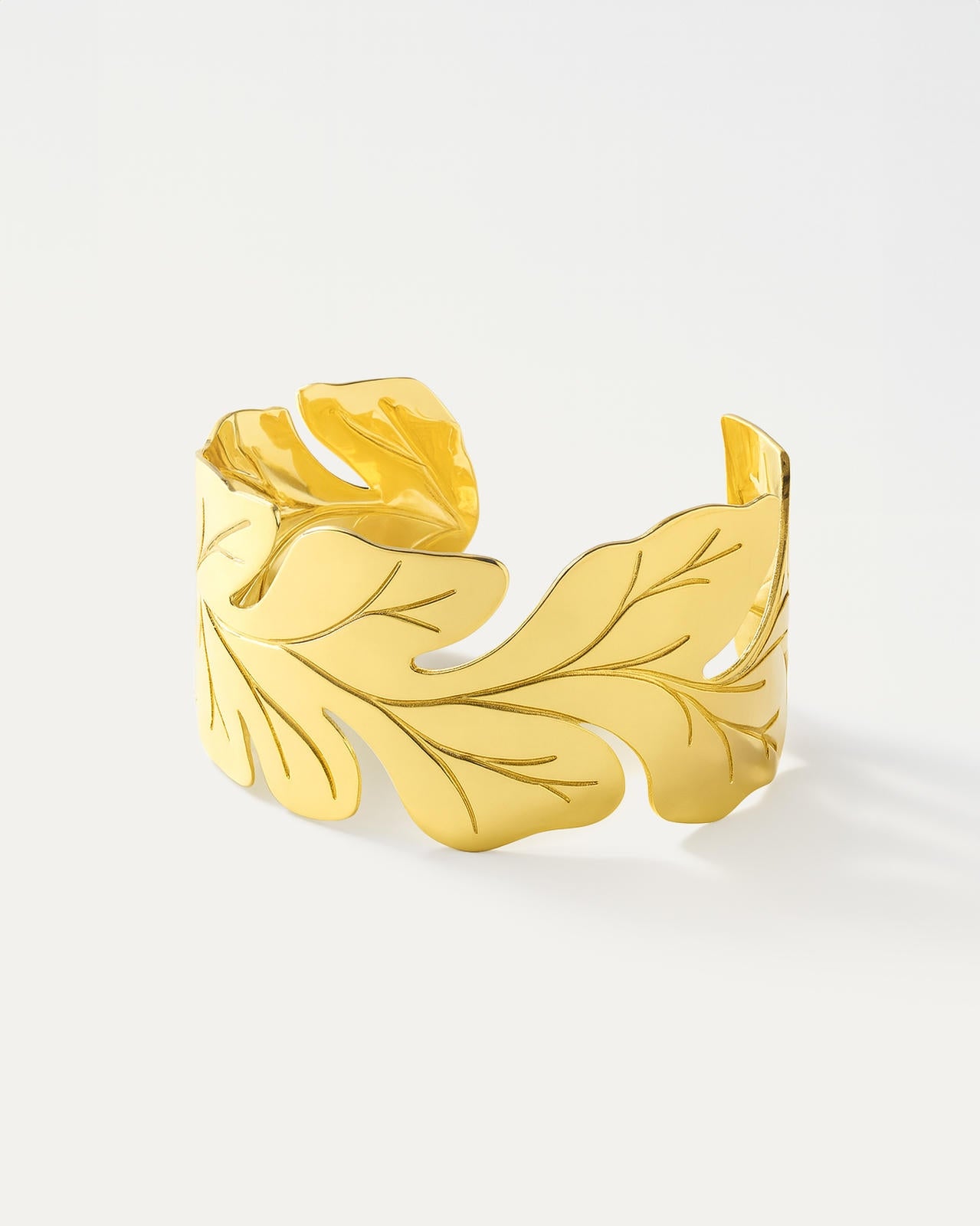A wide, polished gold open-cuff bracelet with a botanical design. The edges are shaped like stylized oak leaves, complete wit