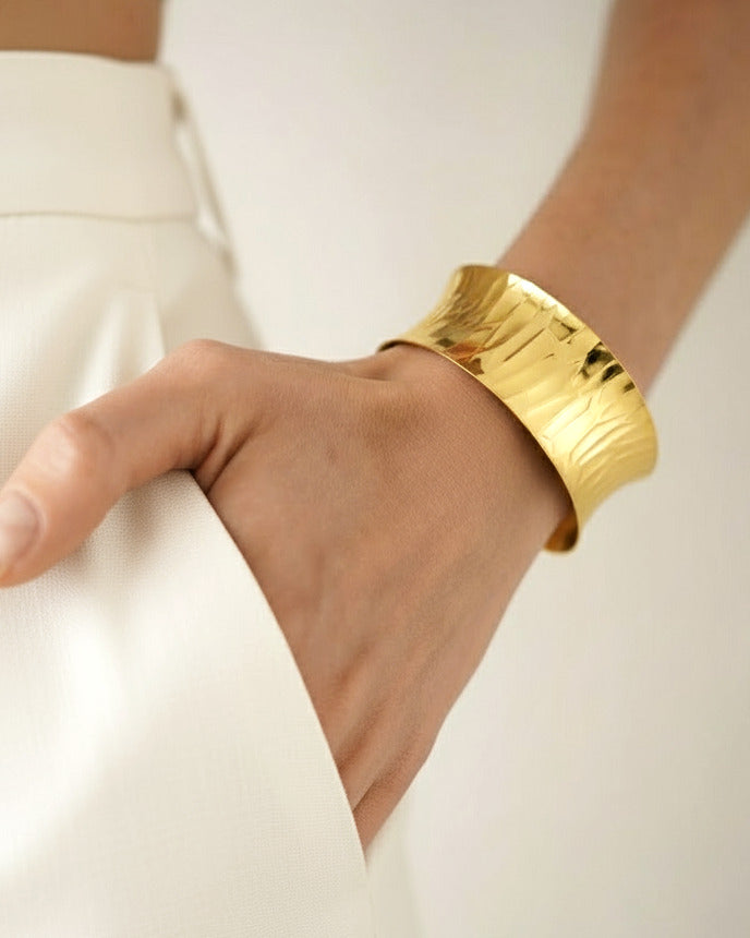 Close-up of model wearing gold hammered cuff bracelet with wide polished surface and minimalist design