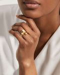 Close-up of a hand wearing a gold ring with a heart design on a neutral background