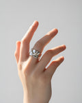 Close-up of a woman's hand against a light background, highlighting a wide, contemporary silver-tone 'Molten Wave Ring' featu