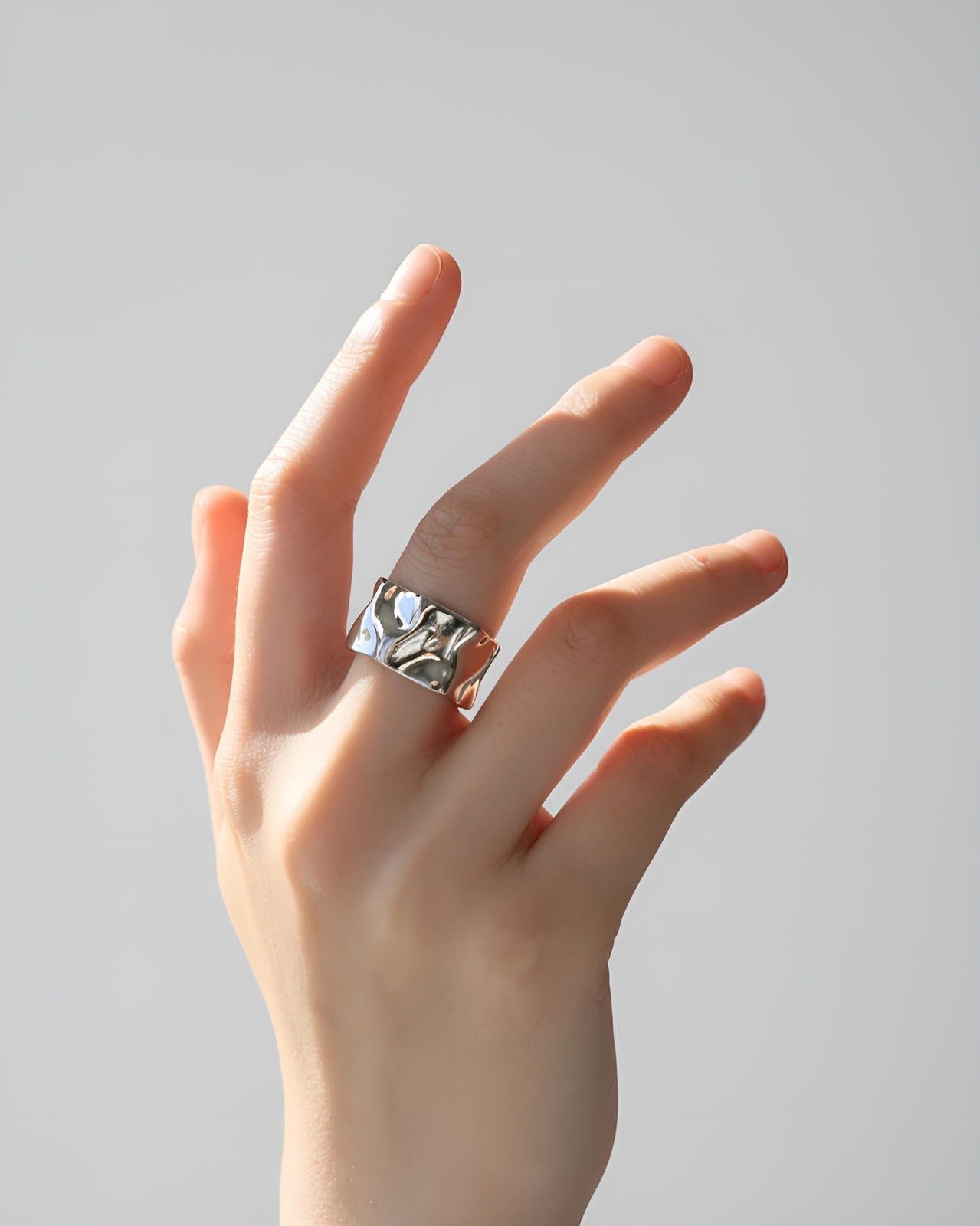 Close-up of a woman's hand against a light background, highlighting a wide, contemporary silver-tone 'Molten Wave Ring' featu