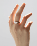 Studio shot of a woman's hand reaching up, highlighting a modern, thick silver-tone band ring with an asymmetrical, curved, a