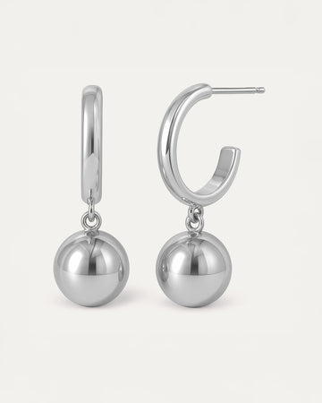 Silver hoop earrings with dangling polished sphere charm in minimalist drop design.