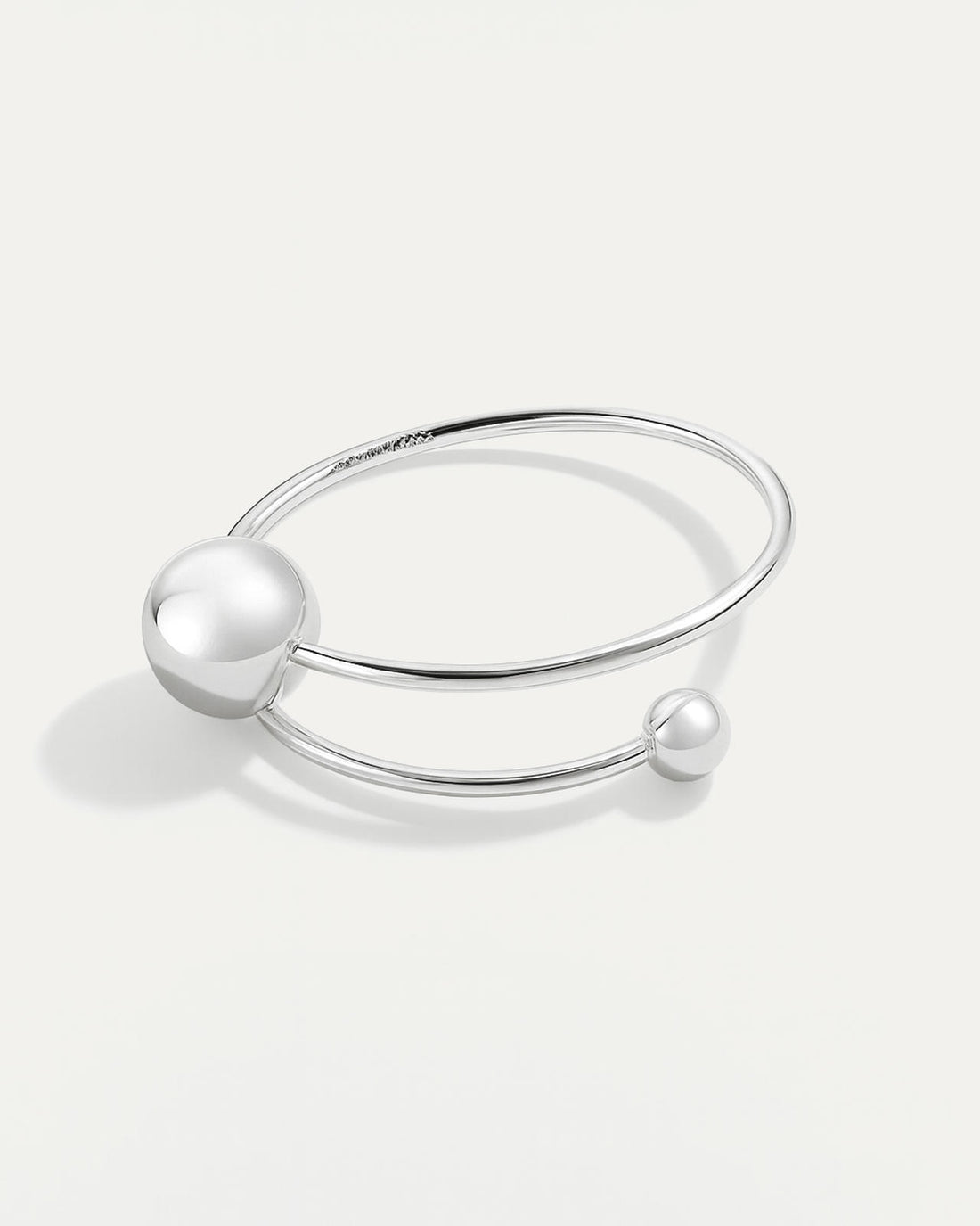 A silver cuff bracelet with a minimalist, open design. It features a smooth, thin band that wraps around, ending in two polis