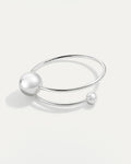 A minimalist, open silver cuff bracelet with a smooth band. The band wraps around, terminating in two polished spheres of con