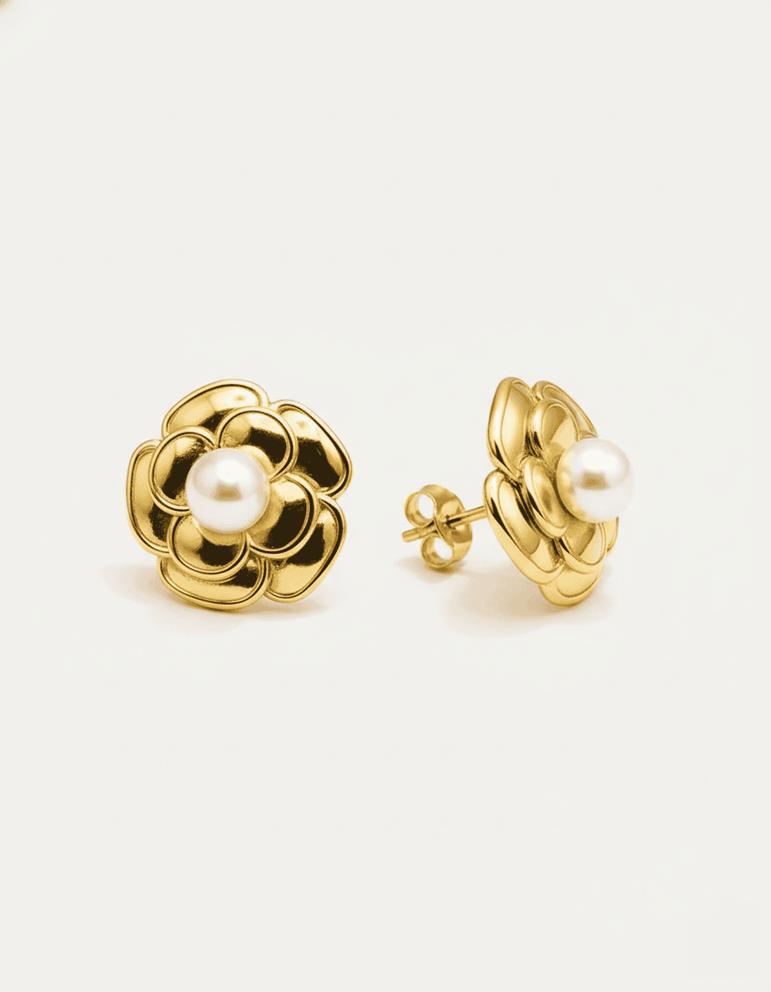 A close-up studio shot of a pair of gold-tone flower stud earrings on a plain white or light beige background. Each earring f