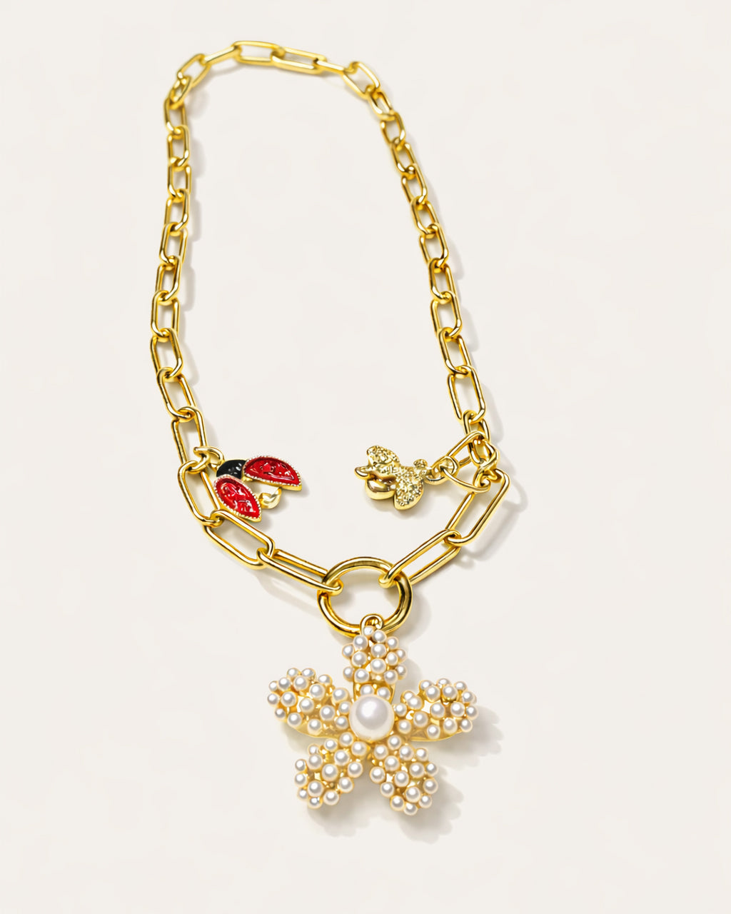 18K gold-plated charm necklace with pearl flower pendant, featuring a bold chain design and decorative charms by Jadejuri