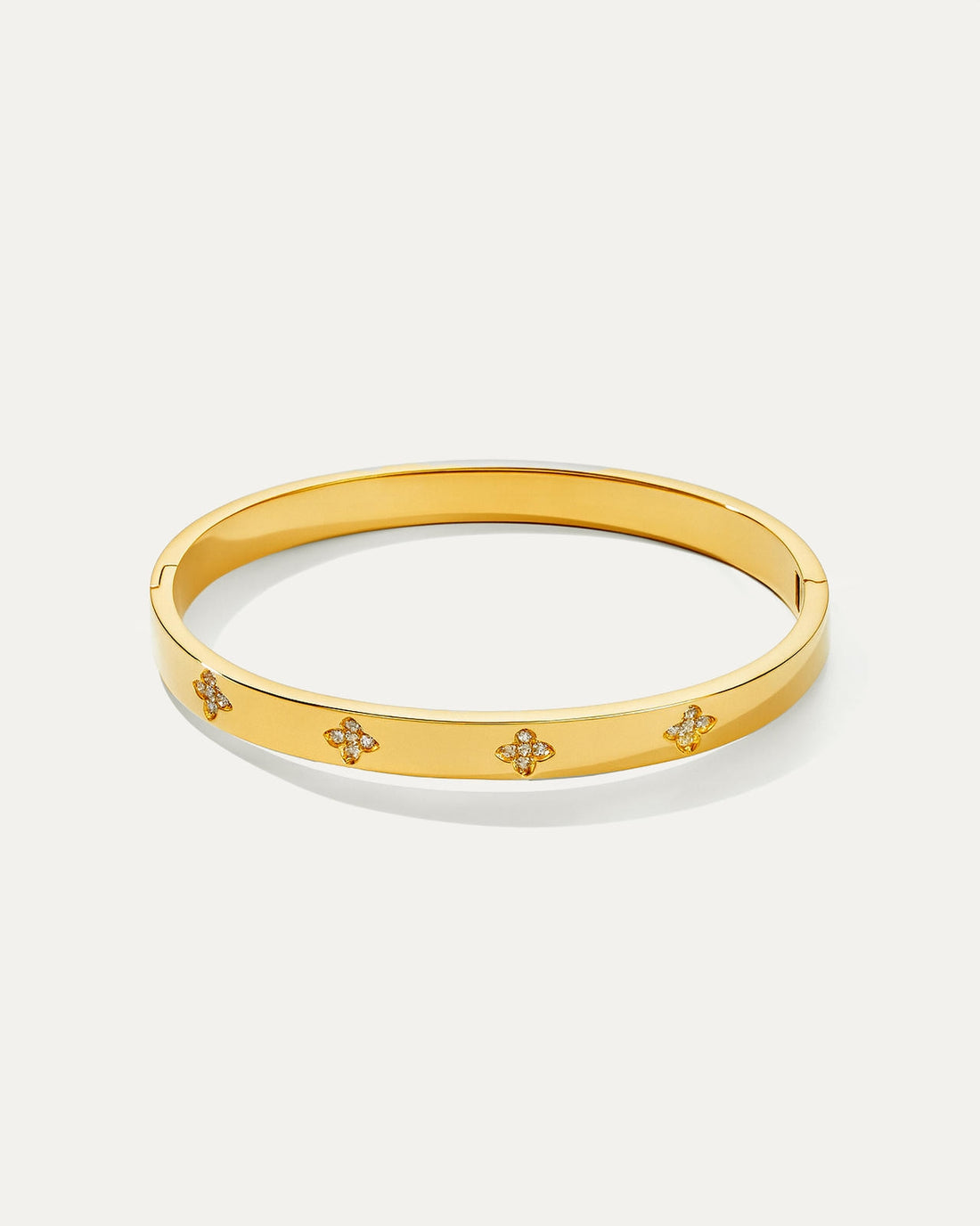 Angled view of a polished gold petite daisy bangle bracelet on a white background, showcasing the slim profile and multiple s