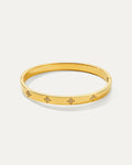 Isolated studio shot of a shiny gold petite daisy hinged bangle bracelet, featuring four evenly spaced, elegant four-leaf clo