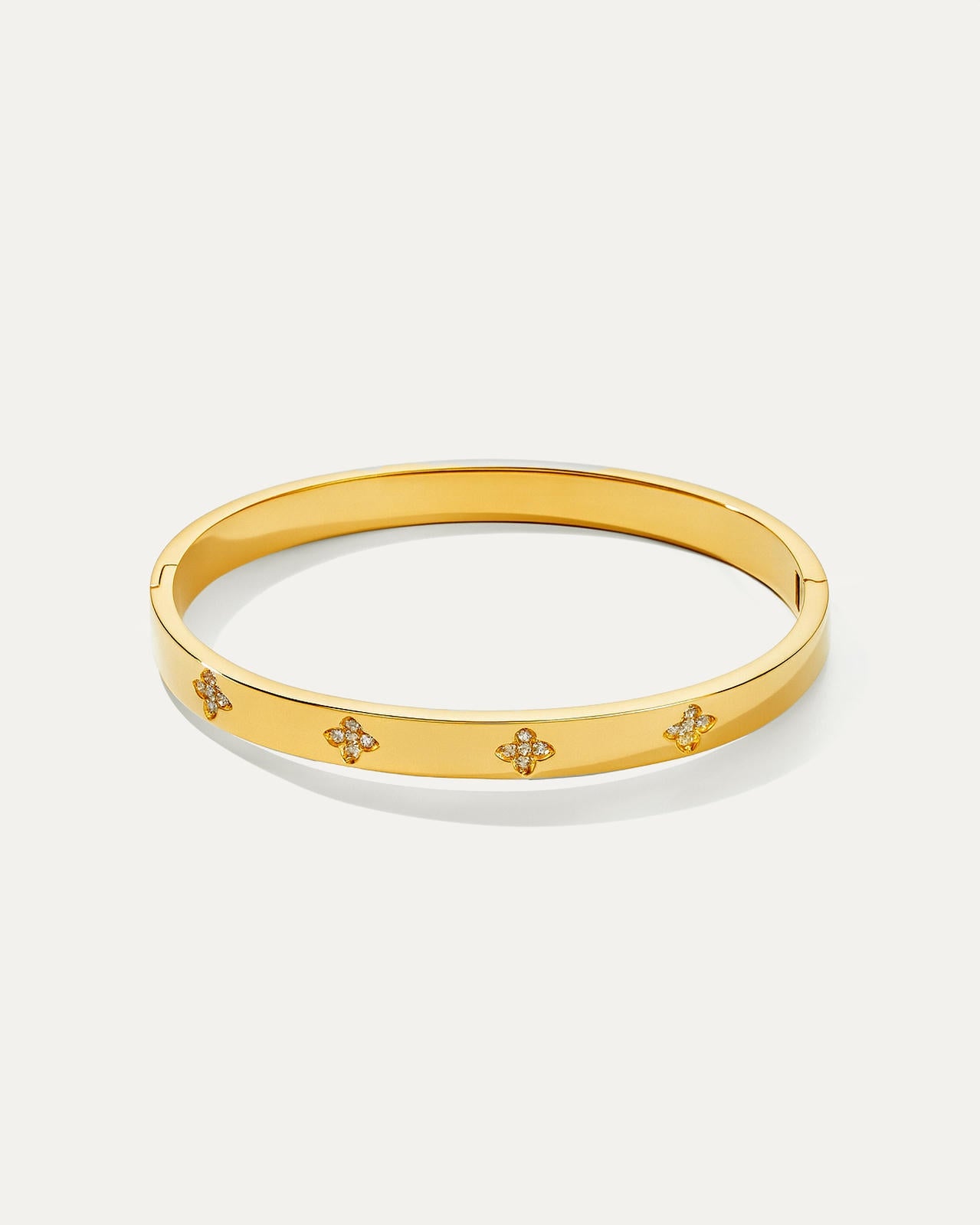 Isolated studio shot of a shiny gold petite daisy hinged bangle bracelet, featuring four evenly spaced, elegant four-leaf clo