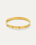 Isolated studio shot of a shiny gold petite daisy hinged bangle bracelet, featuring four evenly spaced, elegant four-leaf clo