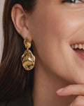 Close-up of abstract gold-plated dangle earrings on model, modern statement style