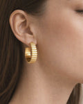 Model wearing gold-plated ribbed hoop earrings with modern textured design