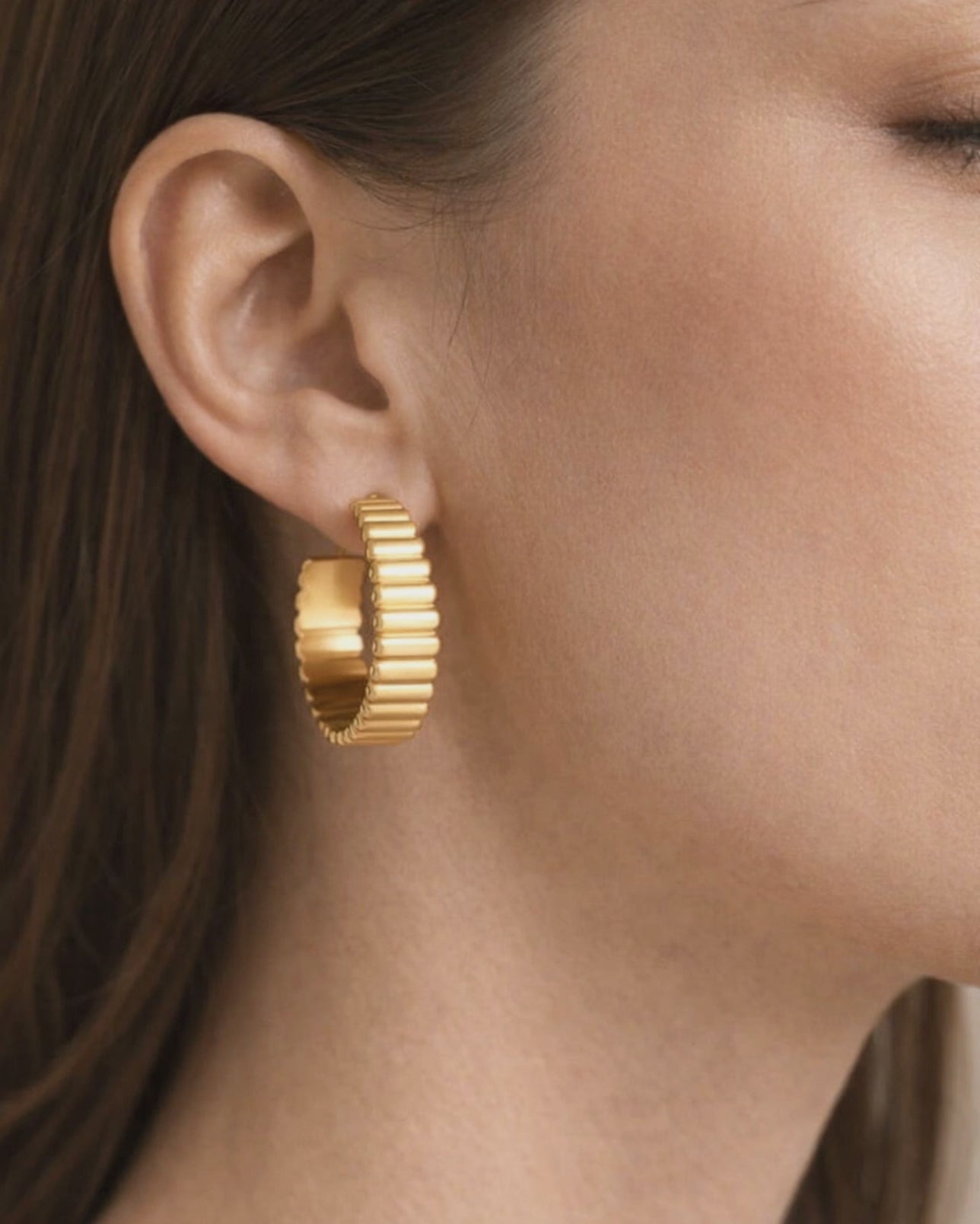 Model wearing gold-plated ribbed hoop earrings with modern textured design