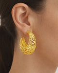 Model wearing gold-plated crescent hoop earrings with ornate cutout design