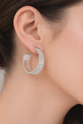 Close-up silver ribbed hoop earrings with bold modern textured design