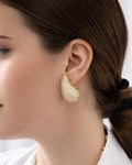 Gold teardrop stud earrings worn on model, featuring a sparkling textured finish and sculptural teardrop shape by Jadejuri