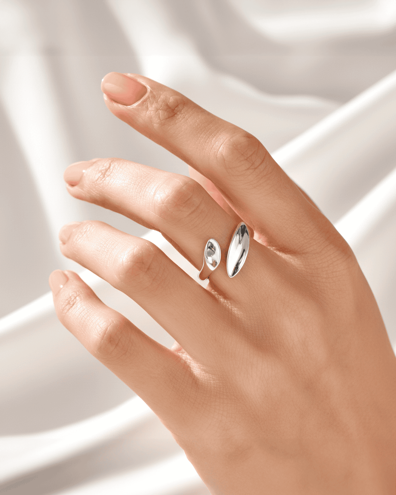 A close-up photograph of a person's hand wearing a silver-tone open cuff ring on their index finger. The ring features two sm