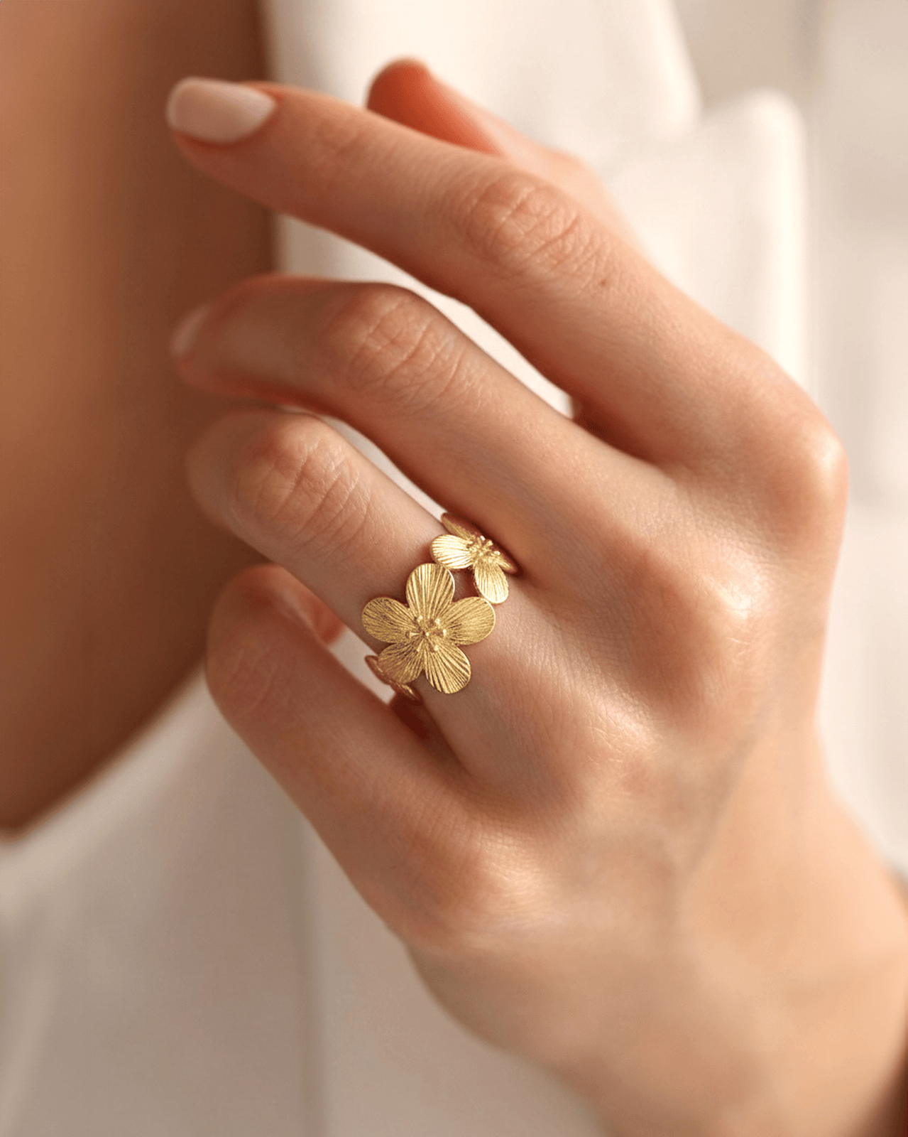 A close-up of a hand wearing a wide gold-tone band ring with a continuous pattern of textured, stylized flowers on the ring f