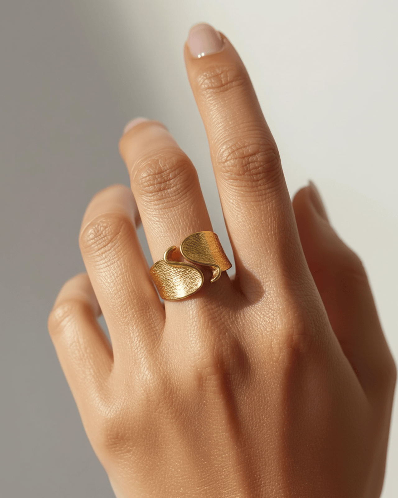 A close-up photograph features a person's hand wearing a bold, sculptural gold-tone ring on their index finger.  