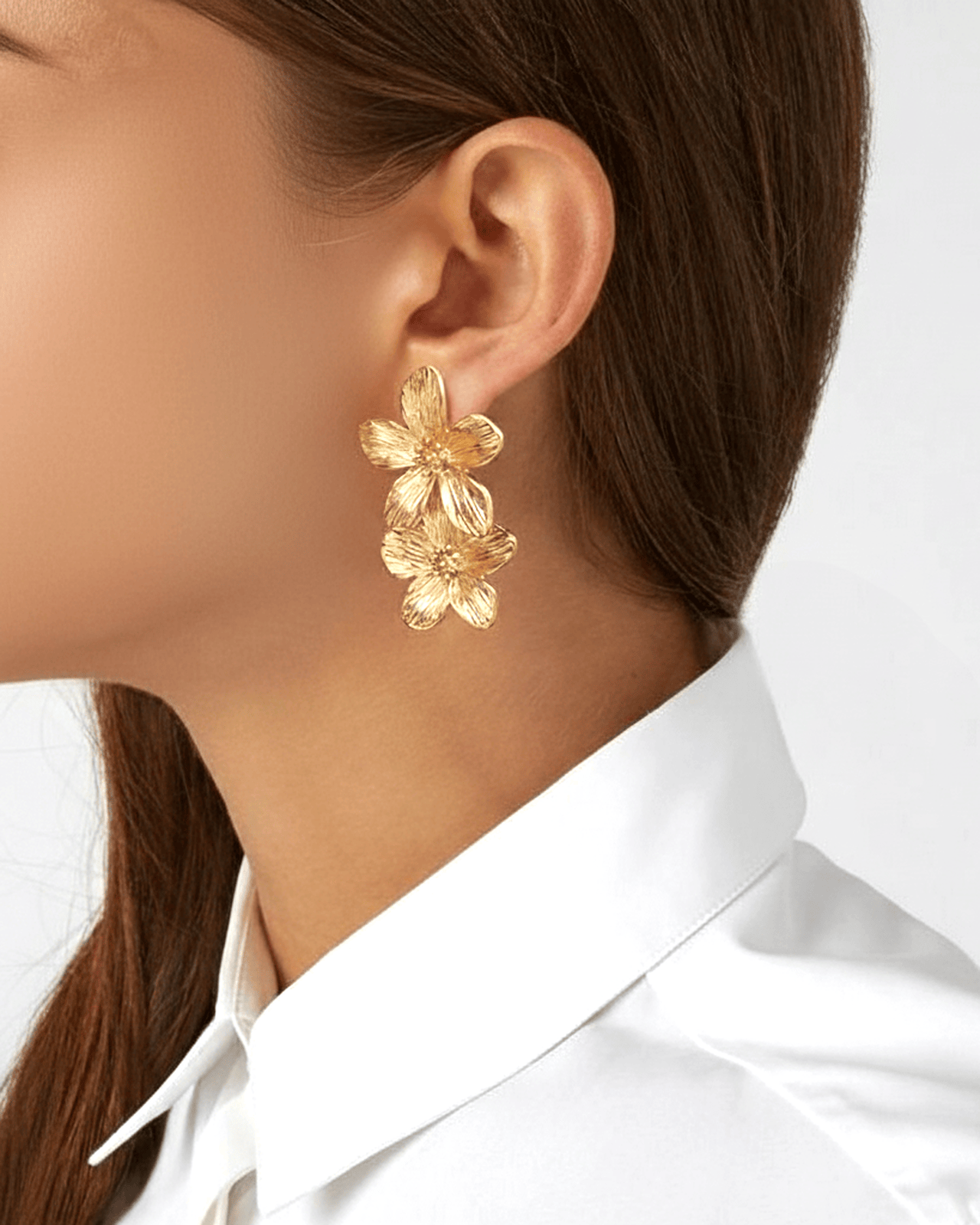 A close-up profile photograph of a woman's ear shows a dangling gold-tone earring with a floral design. The earring consists 