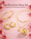 Gold jewelry set including bracelet, earrings, necklace, and ring on a pink floral background with 'The Devotion Muse Set' text.