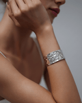 A close-up of a model's arm wearing a wide, statement silver cuff bracelet. The open cuff has a heavily hammered and polished