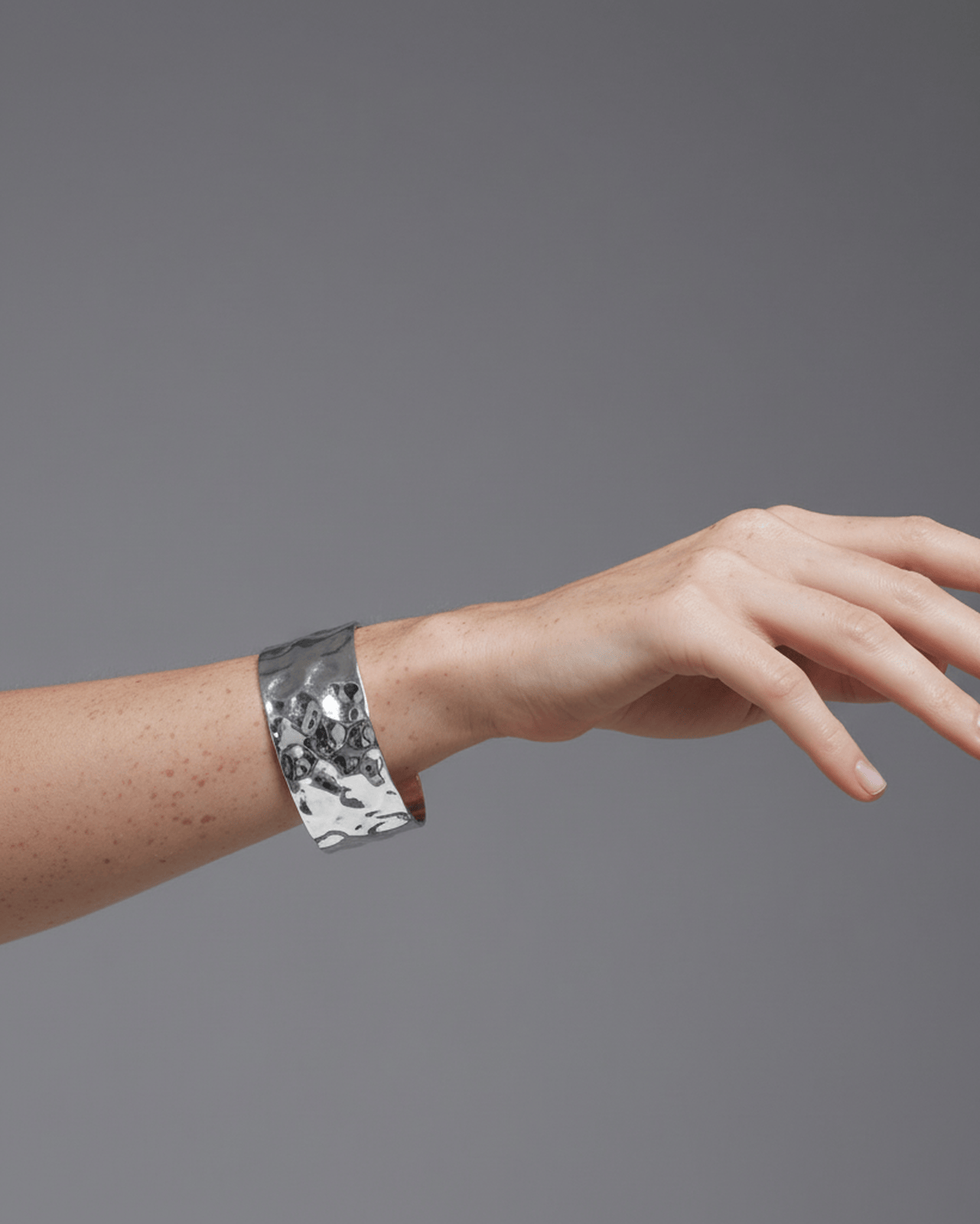 A model's wrist wearing a wide, polished silver open-cuff bracelet. The statement cuff features a pronounced uneven, hammered