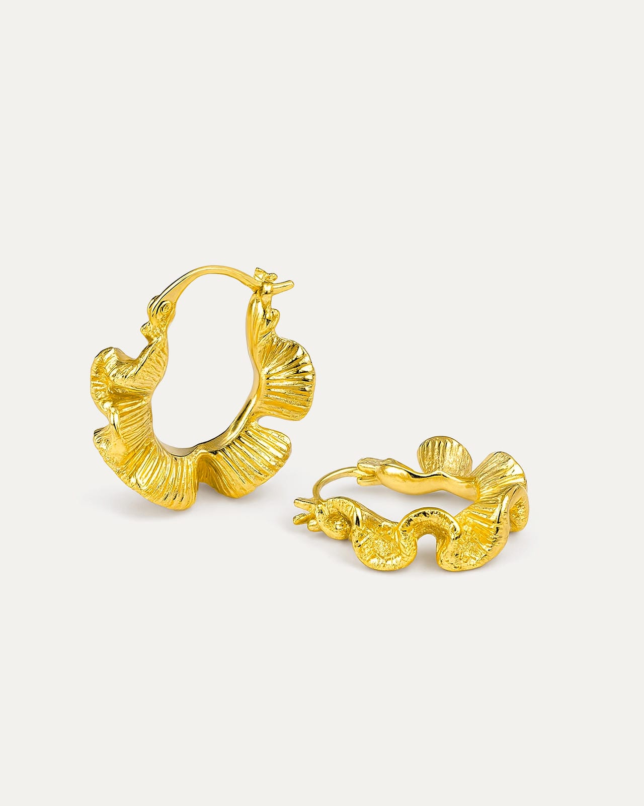 A close-up studio shot of a pair of chunky gold-tone hoop earrings on a plain white or light beige background.  